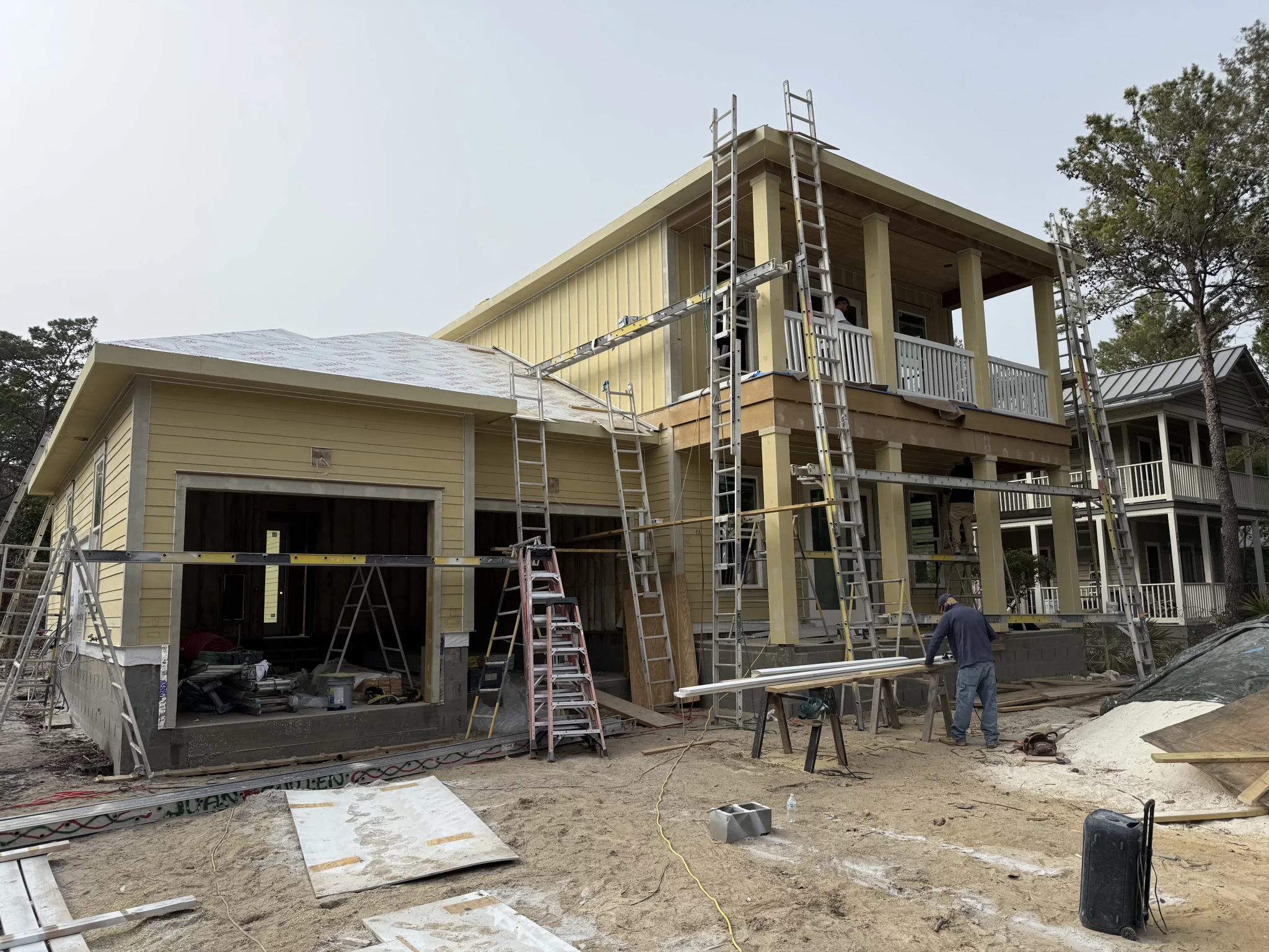 Large two-story house under new construction with scaffolding, ladders, and a worker on a dirt construction site.